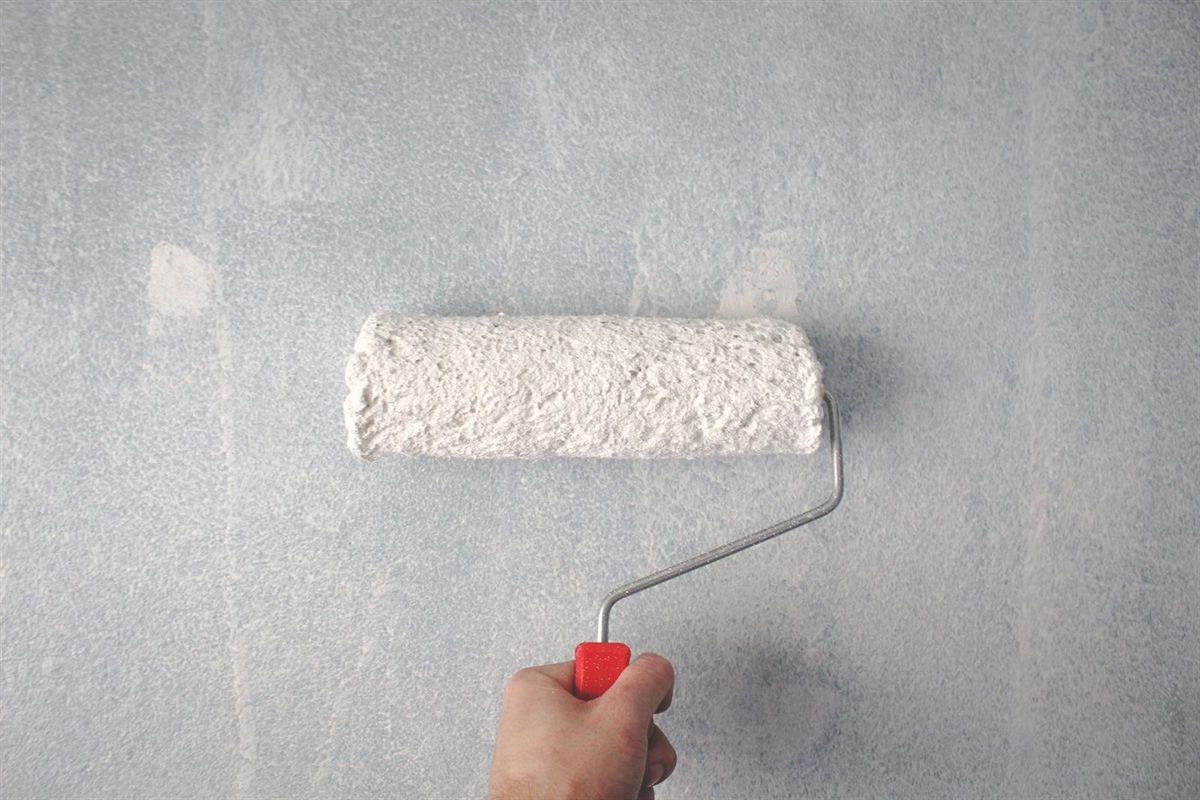 Close-up of a paint roller applying grey emulsion to a wall